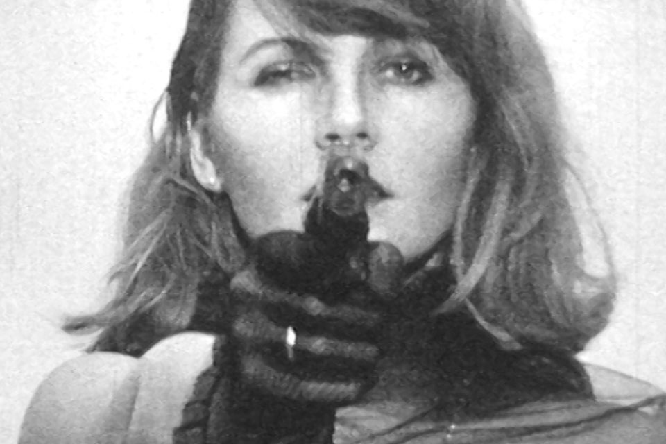 a woman takes aim with a pistol into the camera, video still